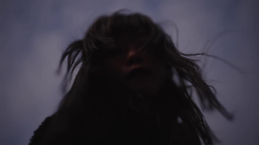 A mysterious woman's hair blows in the wind in slow motion, silhouetted against a cloudy twilight sky