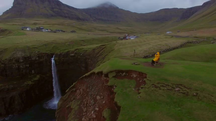 Man in a yellow jacket sits on a bench at the edge of a cliff