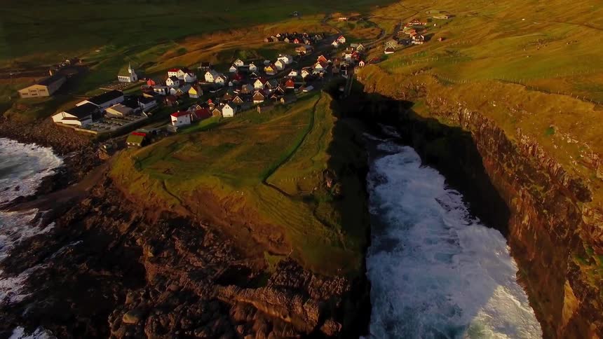 Small group of houses next to crashing ocean waves