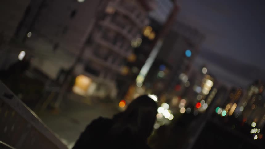 A melancholic woman in a black coat walks away on a city bridge at night, blending into the out-of-focus city lights