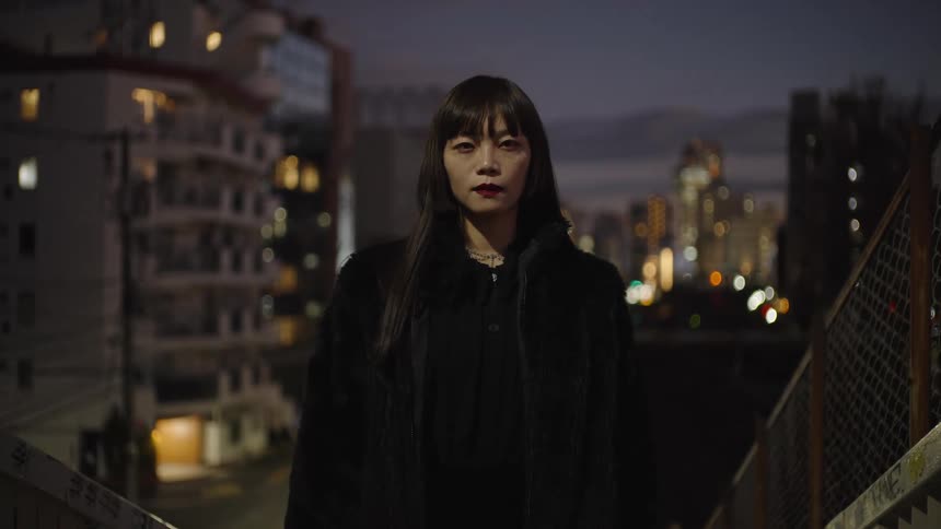 A cinemagraph portrait of a stylish Japanese woman in a black fur coat staring intensely at the camera on a city overpass at night