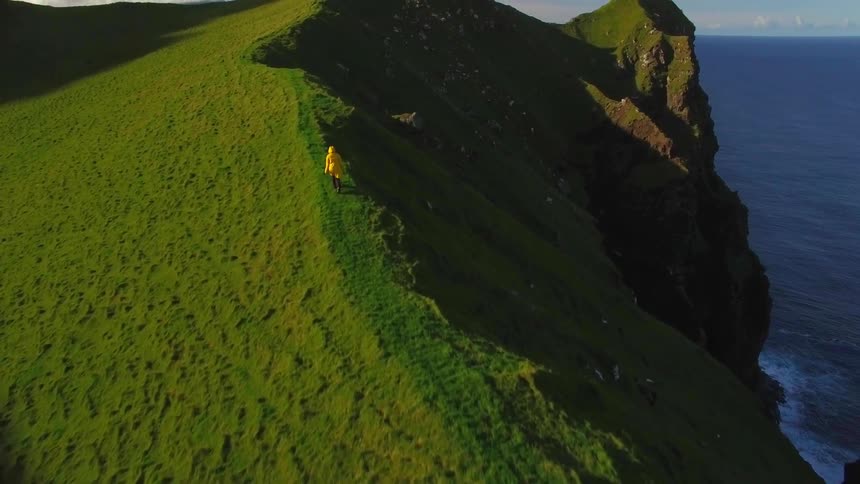 The steep mountain has a person hiking on the edge