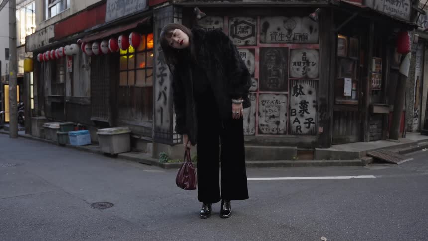 A cinemagraph of a fashionable woman in an all-black outfit posing on an urban street corner in front of a traditional Japanese restaurant