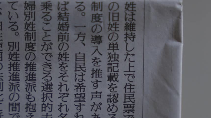 A vertical close-up shot pans across the various articles and advertisements of a Japanese newspaper