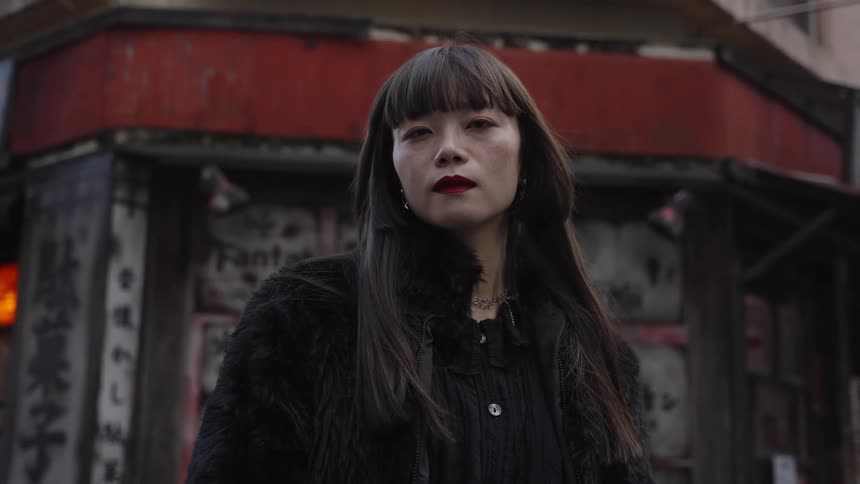 Portrait of a stylish Japanese woman with dark bangs and red lipstick staring intensely on a city street