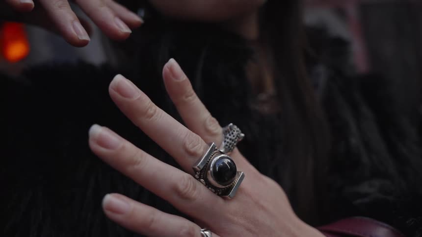 Slow motion close-up of a woman's manicured hands adorned with stylish silver and black stone rings against a dark, moody backdrop
