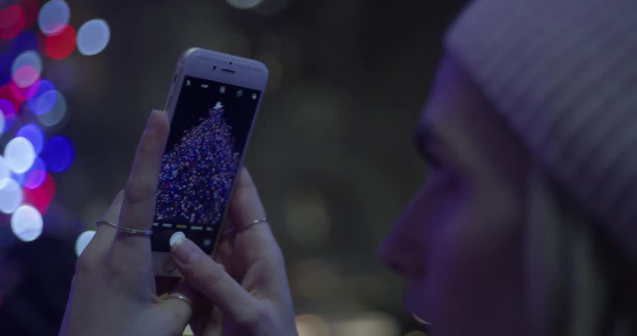 A woman is using her phone to take a photograph of a christmas tree