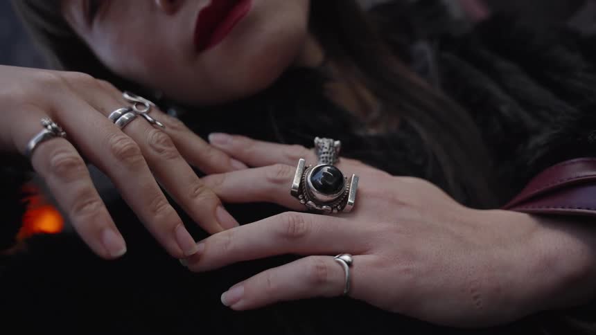 A stylish woman with red lipstick slowly moves her hands, showing off her unique silver rings with black gemstones