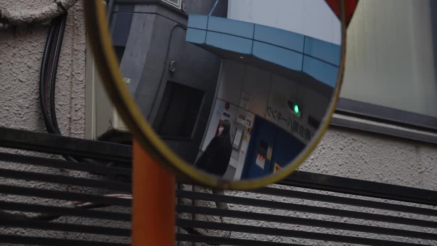 A woman's reflection is captured walking away down a city street in a convex traffic mirror