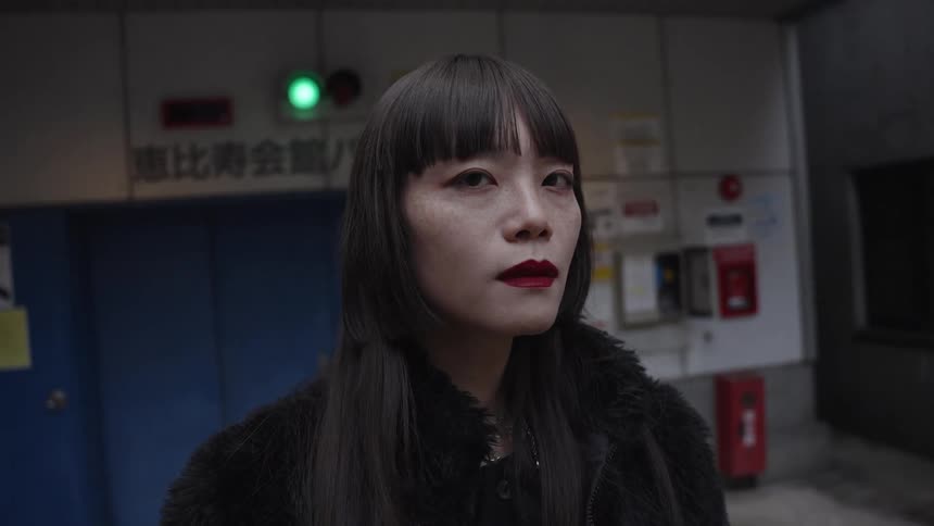 Slow motion close up of a stylish Japanese woman staring intensely into the camera in a dimly lit urban setting