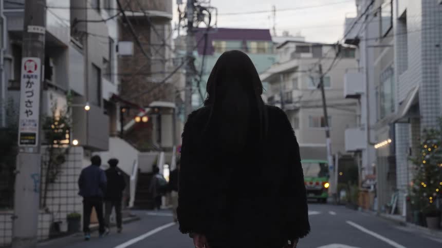 A mysterious woman with long dark hair walks through a quiet city street in Japan in slow motion
