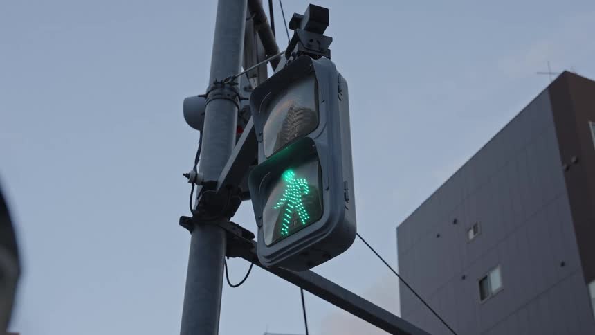 A Japanese pedestrian crosswalk signal changes from a red 'don't walk' sign to a green 'walk' sign in an urban setting