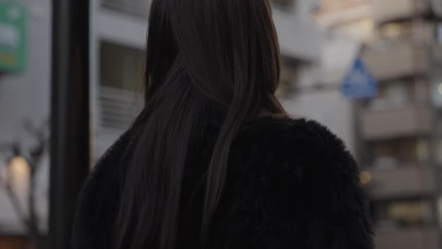 Slow-motion over-the-shoulder shot of a woman with long dark hair walking through a Japanese city street