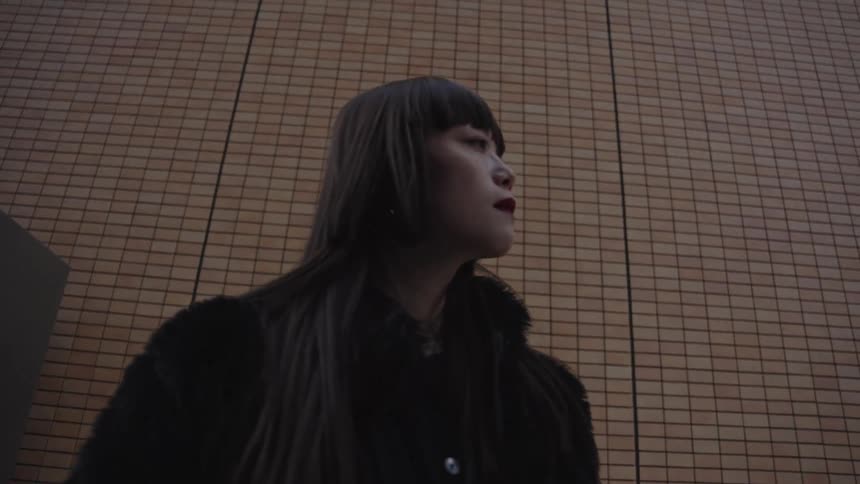 A low angle slow-motion shot of a stylish Asian woman with dark hair standing still against a modern tiled wall