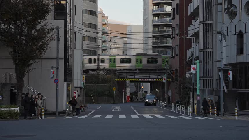 An elevated train passes over a quiet urban street in Tokyo as people go about their day
