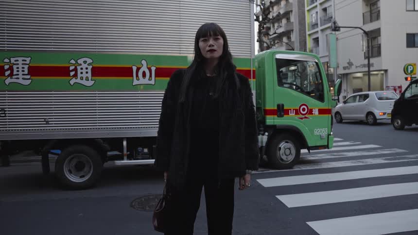 A stylish woman in an all-black outfit poses for a cinemagraph-style portrait on a city street in Japan