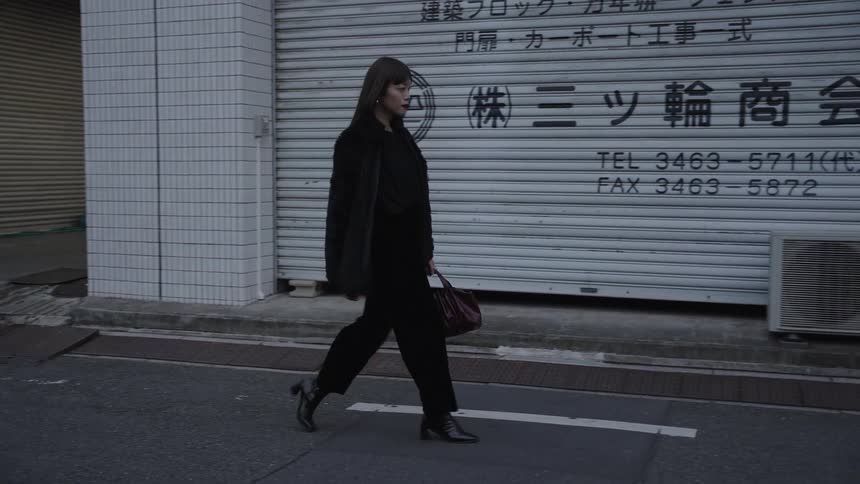 A fashionable woman dressed in black walks in slow motion down a city street in Japan