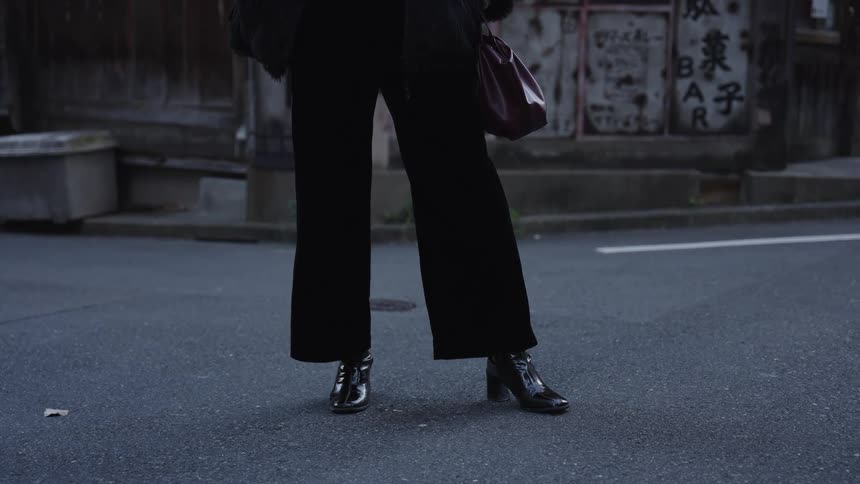 A fashionable person poses on a street in Japan, showing off their black wide-leg trousers and shiny heeled boots