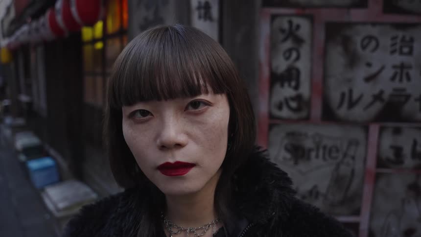 A striking portrait of a Japanese woman with a bob haircut and red lipstick looking directly at the camera in a moody city alley