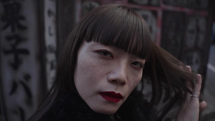 A slow-motion close-up of a stylish Japanese woman with bold red lips and bangs staring intensely into the camera
