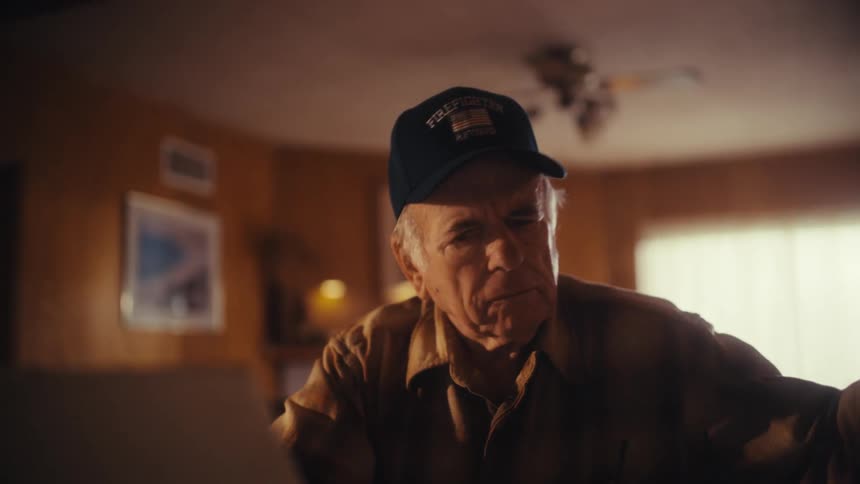 An elderly retired firefighter looks overwhelmed and stressed while trying to manage his finances online at home