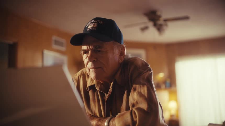 A close-up slow zoom shot of an elderly retired firefighter intently using a laptop in his home