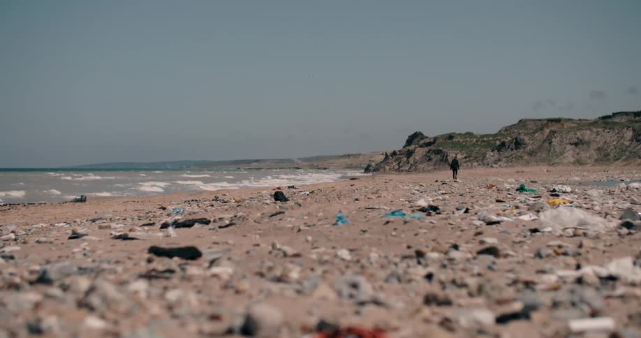 A lone figure walks along a desolate, garbage-strewn beach, highlighting the severe issue of ocean pollution