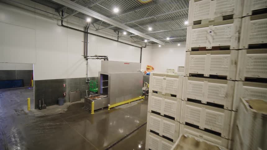 A rising crane shot reveals multiple forklifts organizing and stacking tall columns of white plastic crates in a clean, brightly lit food processing warehouse
