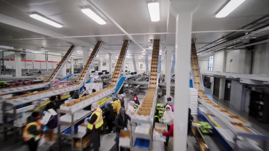 High-angle view moving through a bustling, modern food processing facility with workers and extensive conveyor belt systems