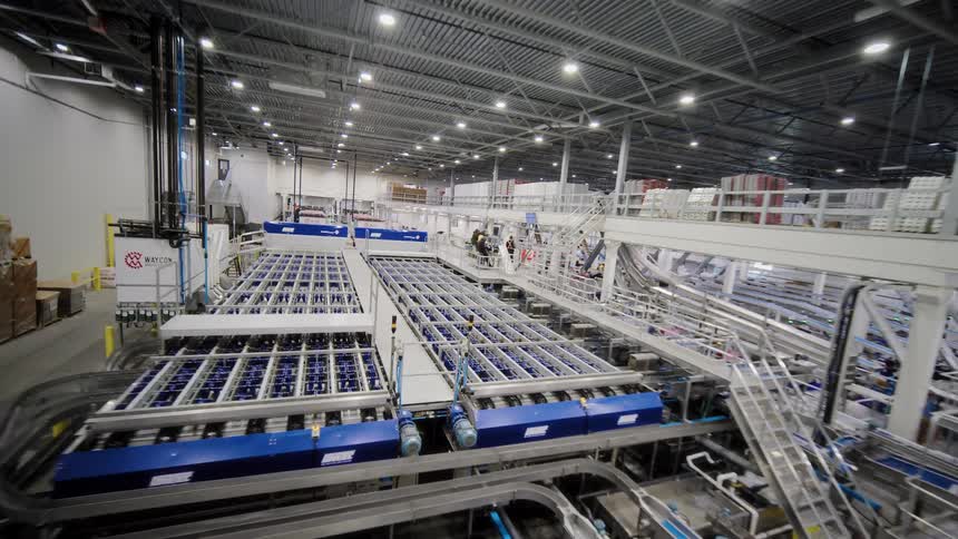 A wide-angle reverse dolly shot reveals the expansive and complex automated machinery of a modern food processing plant