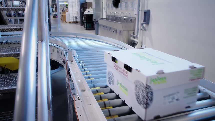 Slow motion shot of branded cardboard boxes moving along a roller conveyor belt inside a clean, modern food packaging facility