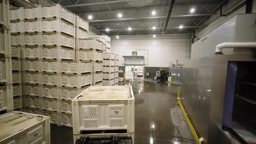 Following a forklift operator as they move stacks of large plastic crates through an industrial warehouse facility