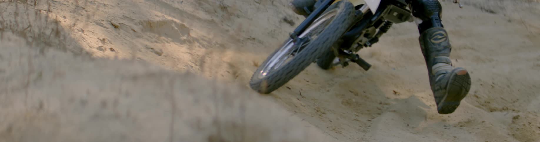 Person rides dirt bike on a sandy beach on a sunny day