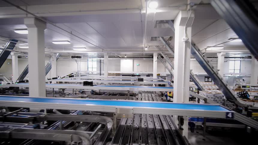 An expansive, automated industrial facility is revealed in a slow pull-back shot, showcasing its intricate network of conveyor belts and machinery
