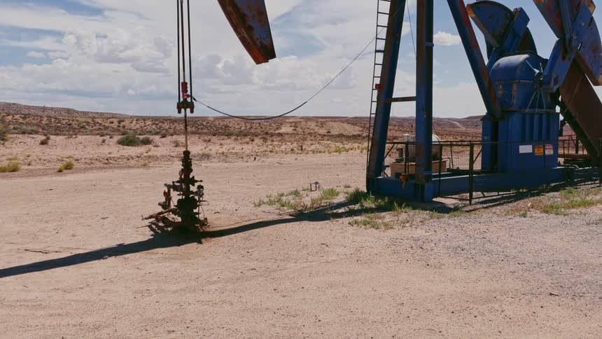 An oil pump jack rhythmically extracts crude oil from the ground in the vast, arid desert landscape