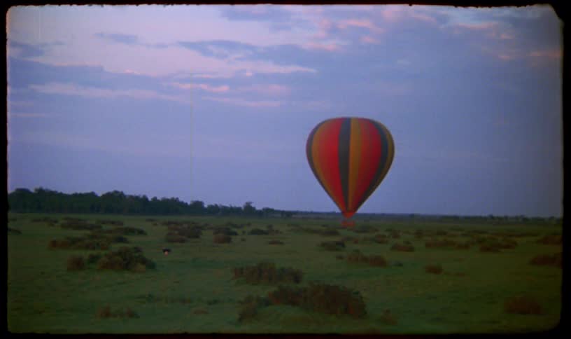 A colorful hot air balloon rests in a vast green field at twilight in this serene vintage footage