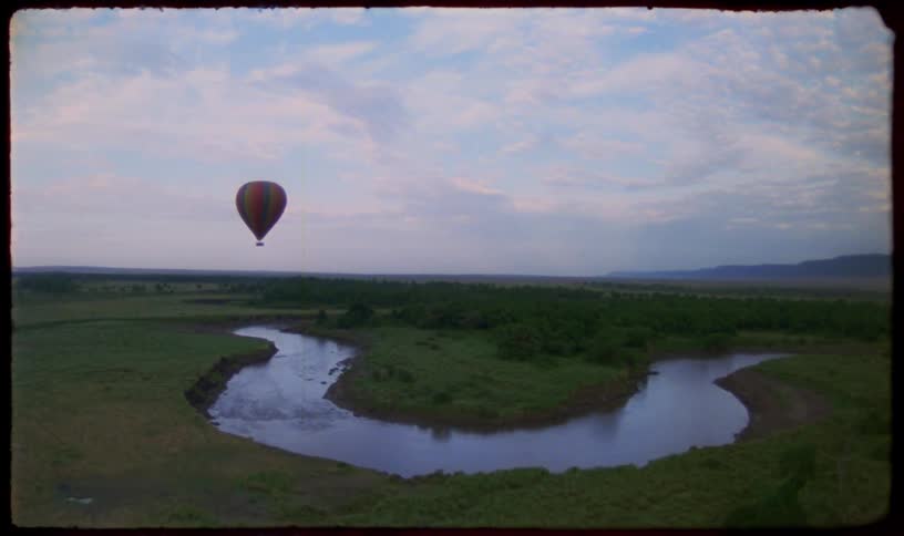 Vintage footage shows a colorful hot air balloon floating over a winding river in the vast African savanna