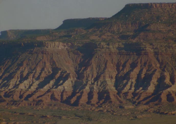 A static shot shows the rugged, eroded rock formations of multi-colored mesas in a vast desert landscape