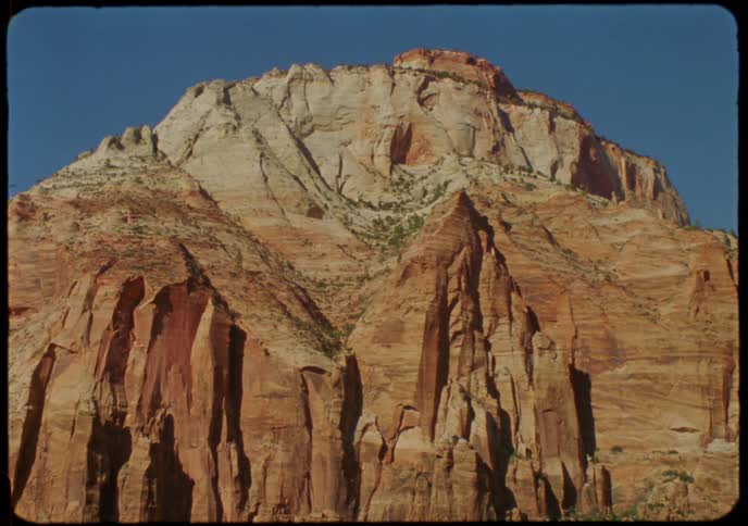Vintage film captures a static, majestic view of a massive red and white rock mountain in a national park under a clear blue sky