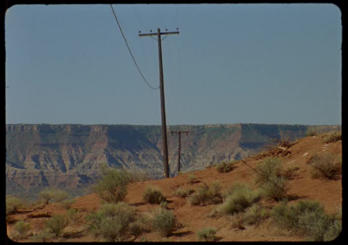 A slow zoom on rustic telephone poles set against a vast desert canyon backdrop, captured on vintage Super 8 film