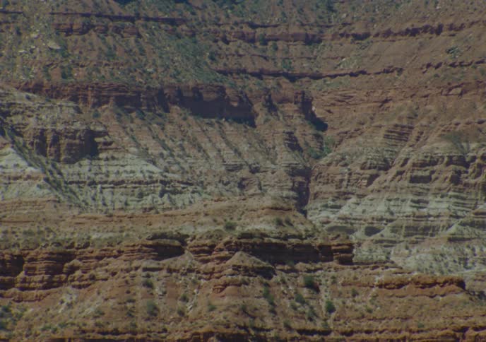 A static close-up shot showcases the colorful, stratified rock layers of an arid canyon wall