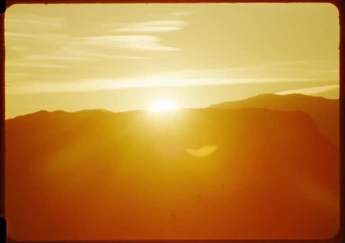 A vintage 8mm film captures the warm golden glow of a sunrise over a hazy mountain range