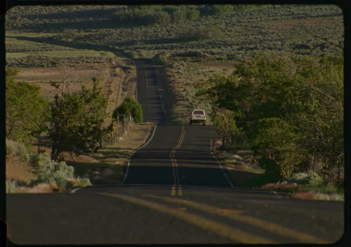 A single car drives away down a long, winding country road in this vintage-style shot