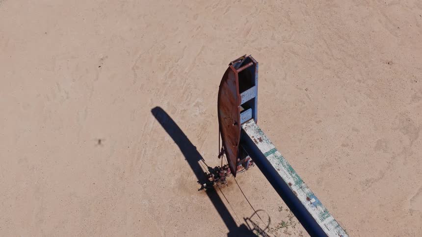 Top-down aerial shot of a rusty oil pumpjack operating in a vast, arid landscape