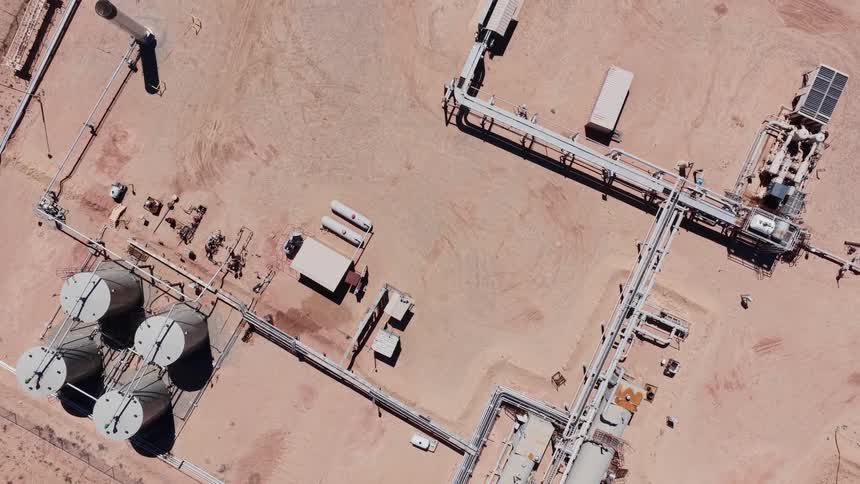 A top-down aerial shot slowly rises to reveal a remote oil and gas processing facility in the middle of a desert