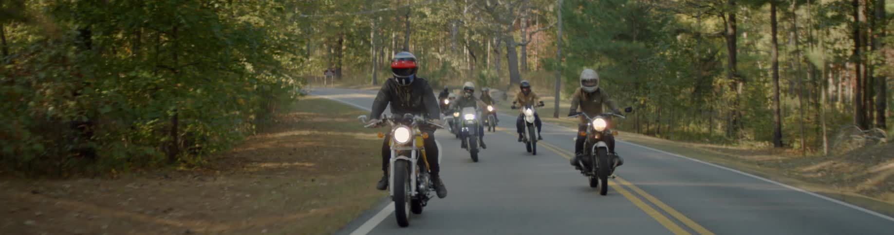 A group of motorcyclists are riding their bikes in a forested area