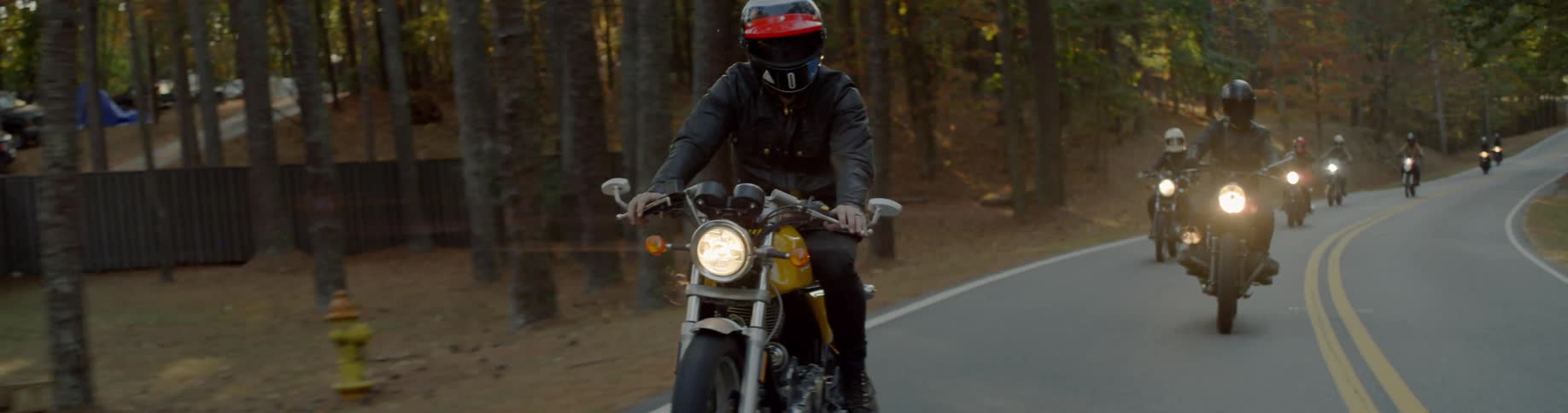 Group of people riding motorcycles on a tree lined road