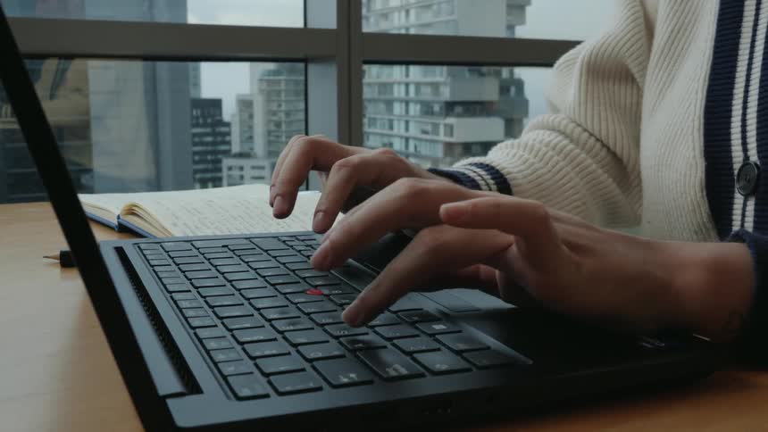 A close-up of hands swiftly typing on a laptop keyboard, set against the backdrop of a modern cityscape