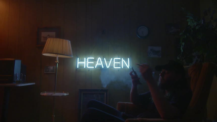 A man sits in a chair and smokes while looking at his cellphone