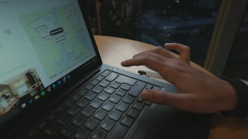 A person's hands type and scroll on a laptop, browsing a travel accommodation website at a table in the evening